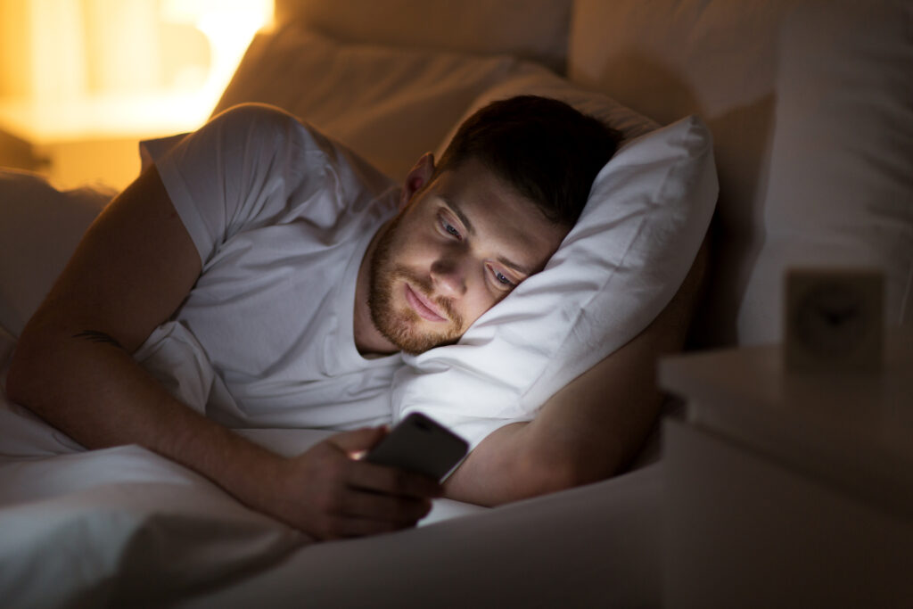 Mann schaut im Bett auf den hellen Bildschirm des Smartphones