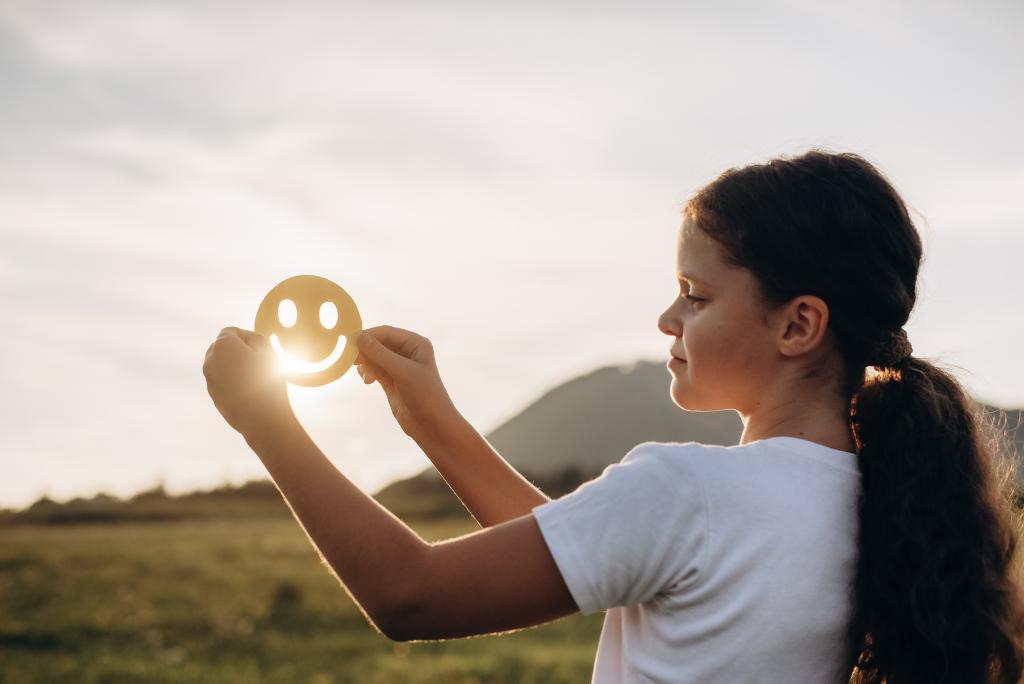 Eine Frau hält einen Papier-Smiley in die Luft.